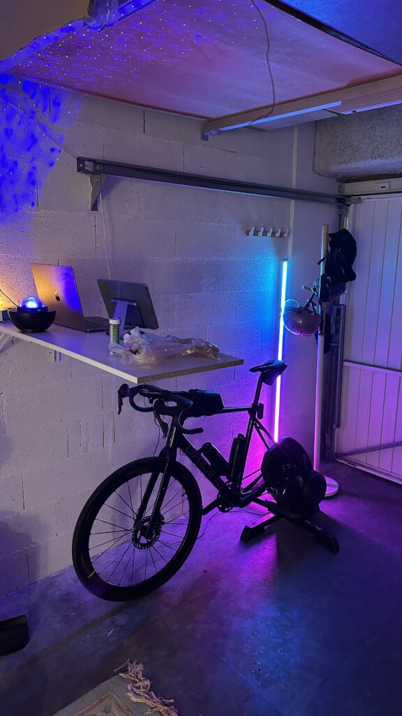 Photographie de mon ancien setup vélo home trainer installé dans mon garage. Vélo Origine Graxx III monté sur home trainer Elite Direto XR avec le Zwift Cog and Click. Utilisé pour mes entraînements cyclisme et préparation triathlon à domicile.
